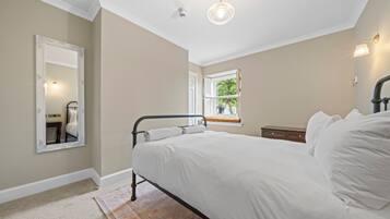Un dormitorio con cama, mesita de noche, cómoda, espejo y ventana con vista a la vegetación.