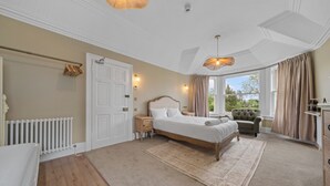 Une chambre à coucher avec un grand lit, une chaise, un radiateur, une fenêtre avec des rideaux et un lustre.