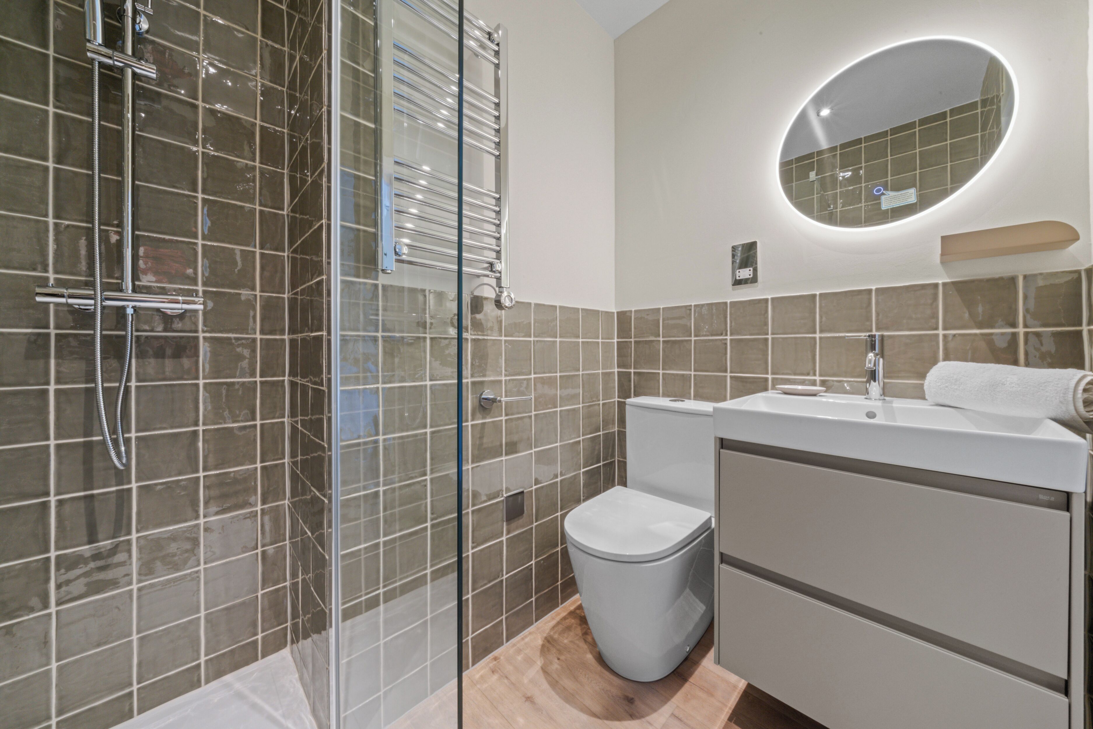 A modern bathroom with a glass shower enclosure, a toilet, a sink with a mirror above, and a towel rack.