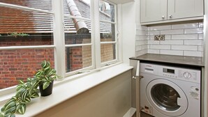 Een kleine wasruimte met een Bosch wasmachine, een raam met zonwering en een bloempot op de vensterbank.