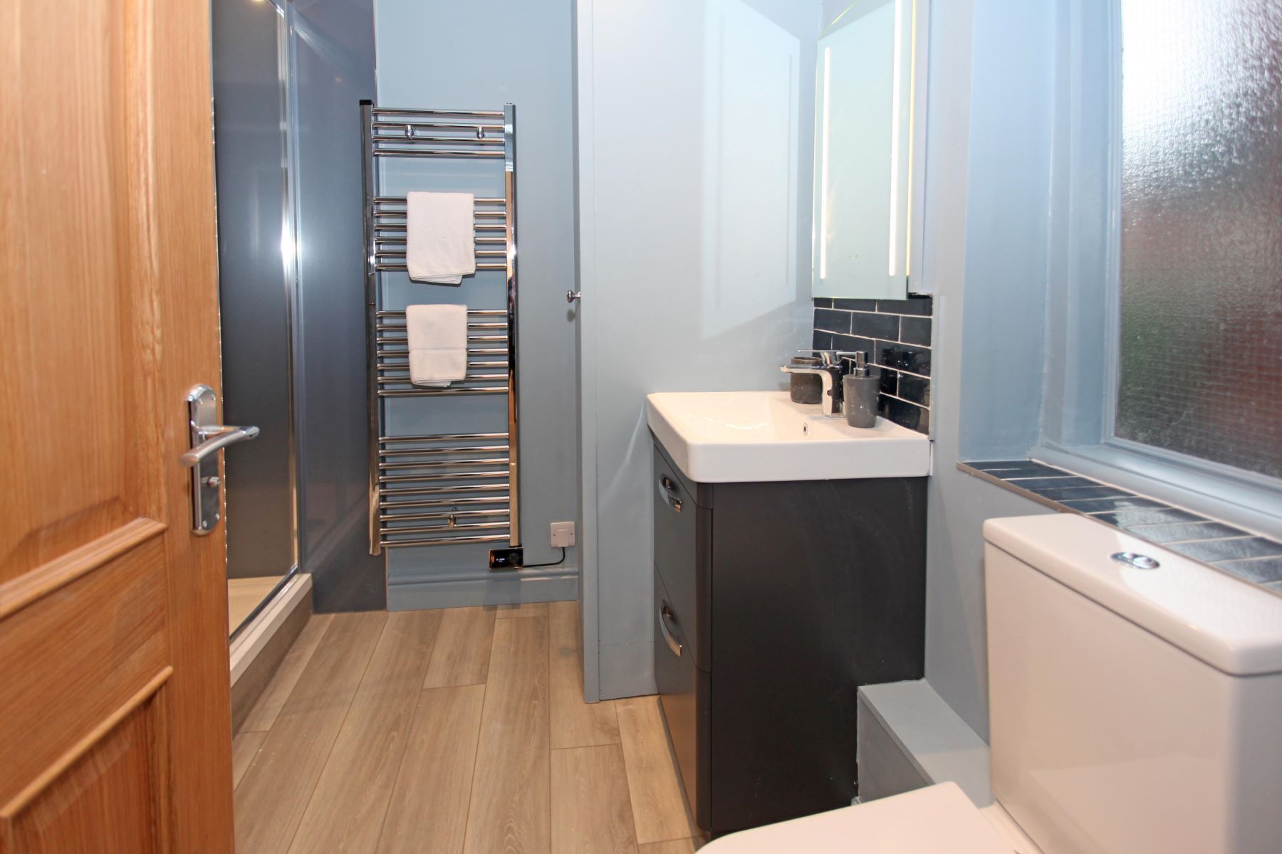 Une petite salle de bain avec une porte en bois, un porte-serviettes avec deux serviettes, un lavabo avec un miroir et des toilettes.