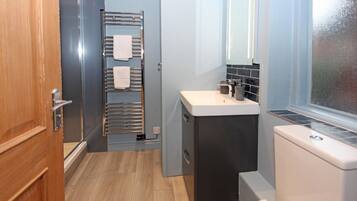 Une petite salle de bain avec une porte en bois, un porte-serviettes avec deux serviettes, un lavabo avec un miroir et des toilettes.