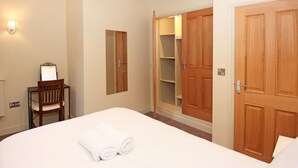 Hotelkamer met een bed, een stoel, een bureau met spiegel, een kledingkast en een openstaande kast met planken.