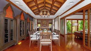 A spacious dining area with a high wooden ceiling and a chandelier, surrounded by traditional cabinets and a large window with a view of greenery. - Royal Legacy Golf Villa (Rawai)