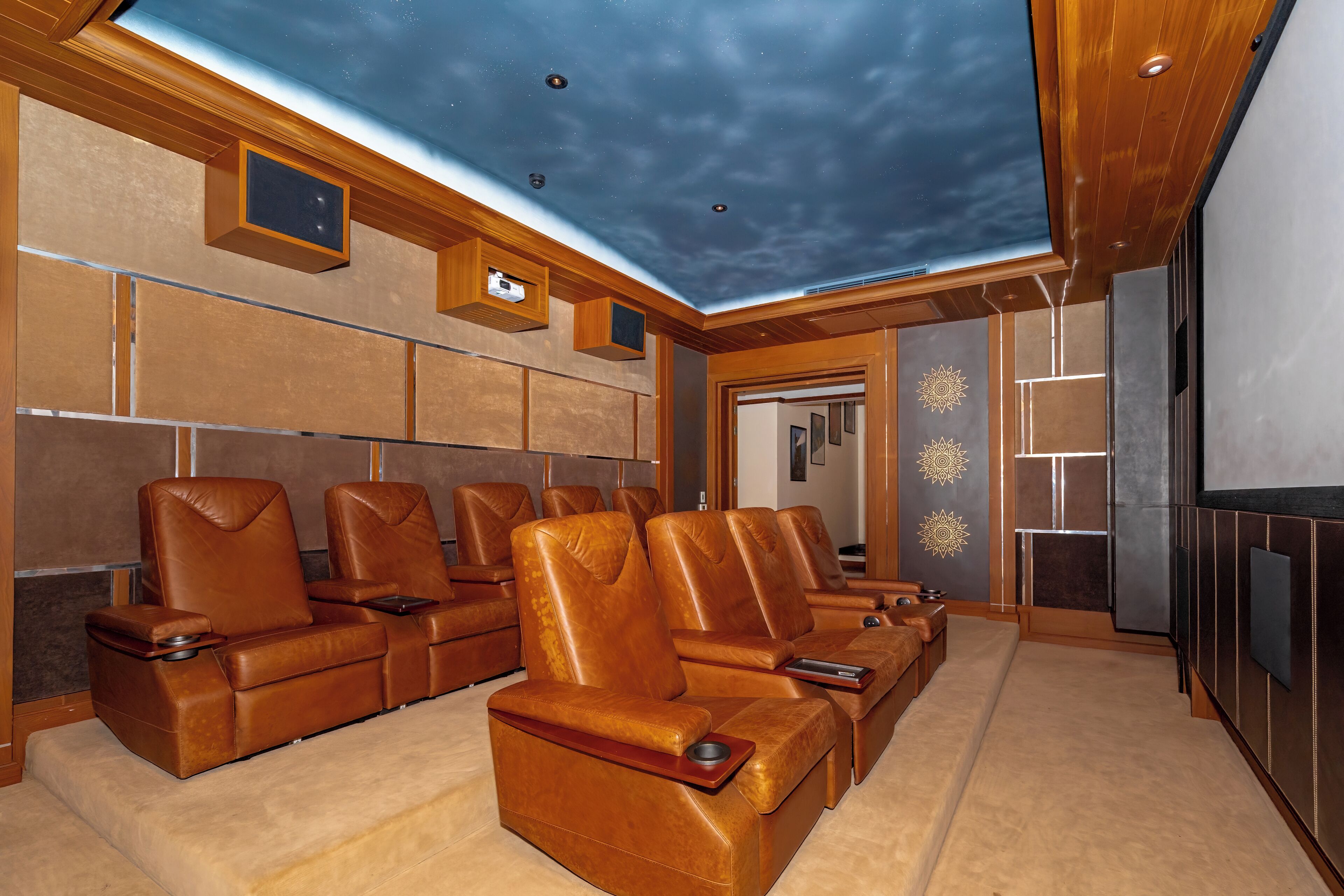 Sala de cinema com poltronas reclináveis de couro, uma tela grande e um design de teto que imita um céu estrelado.