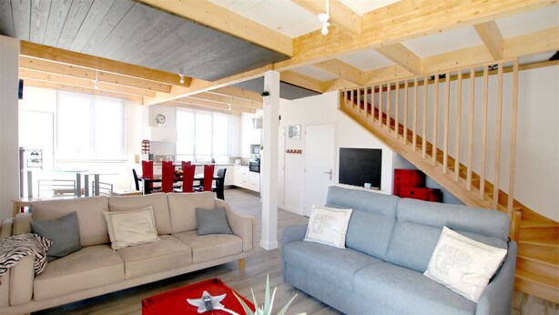 Ein großzügiges Wohnzimmer mit hoher Decke, einer Treppe und einem Essbereich im Hintergrund.