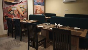 A dining area with booths and tables, air conditioning, and a wall with food posters. - Raj Hotel By Rao (Udaipur)
