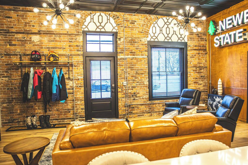 A cozy room with a leather sofa, a coffee table, and a seating area with a chair. There is a coat rack with jackets and a door with windows.