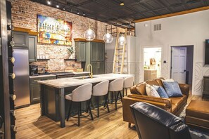 A modern kitchen with a brick wall, bar stools, and a wooden dining table.