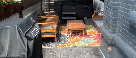 An outdoor patio with a barbecue grill, seating area, and a patterned rug.