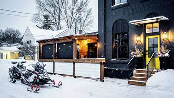 Et snedækket boligområde med et hus, der har en træveranda, en gul dør og en garage. Der er sne scootere parkeret foran.