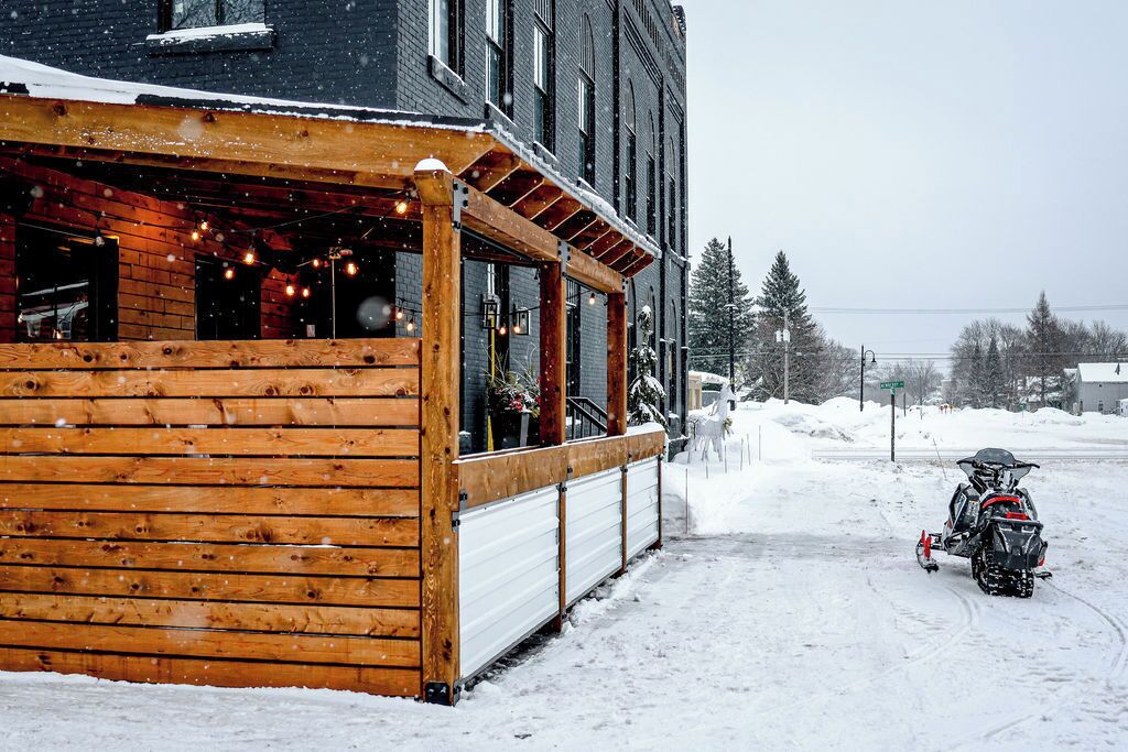 A wooden building with a covered outdoor area and a snow-covered street.