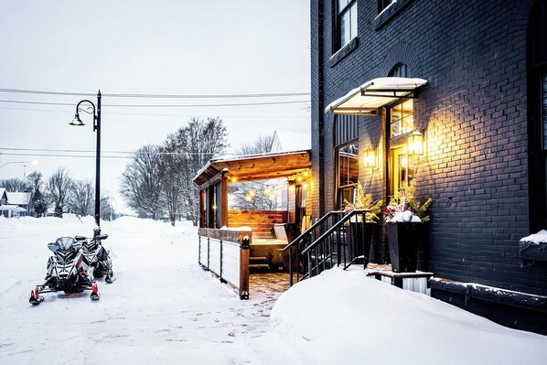 A snow-covered path leading to a wooden cabin-style building with a porch and outdoor seating area.