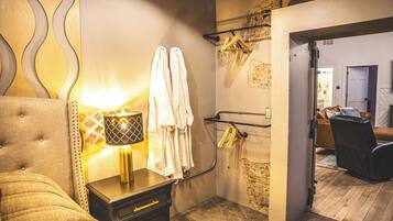 A hotel room with a tufted headboard, a bedside lamp, a wardrobe, a towel rack, and a mirror.