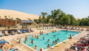 A swimming pool area with lounge chairs and a desert landscape in the background. - Camping de la Dune (La Teste-de-Buch)