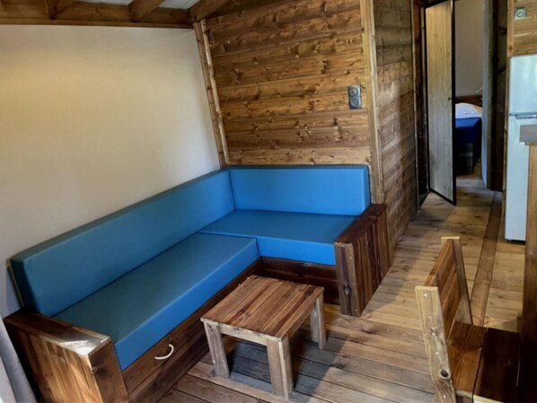 A wooden interior with a blue cushioned bench and a small wooden table. - Camping de la Dune (La Teste-de-Buch)