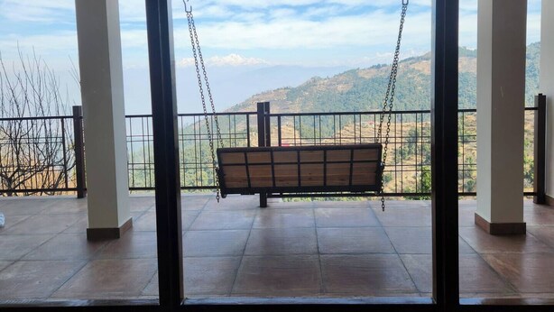 Un balcon agrémenté d’une chaise suspendue en bois, d’où l’on peut admirer un paysage montagneux.