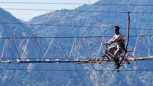 Une personne à vélo traverse un pont suspendu, avec un paysage montagneux en arrière-plan.