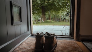 A pair of boots on a doormat in front of a door with a view of a backyard.