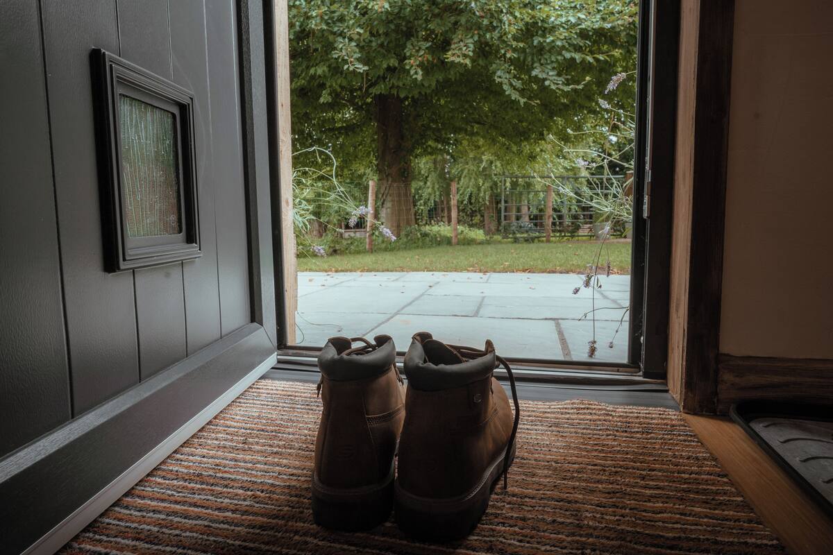 A pair of boots on a doormat in front of a door with a view of a backyard.