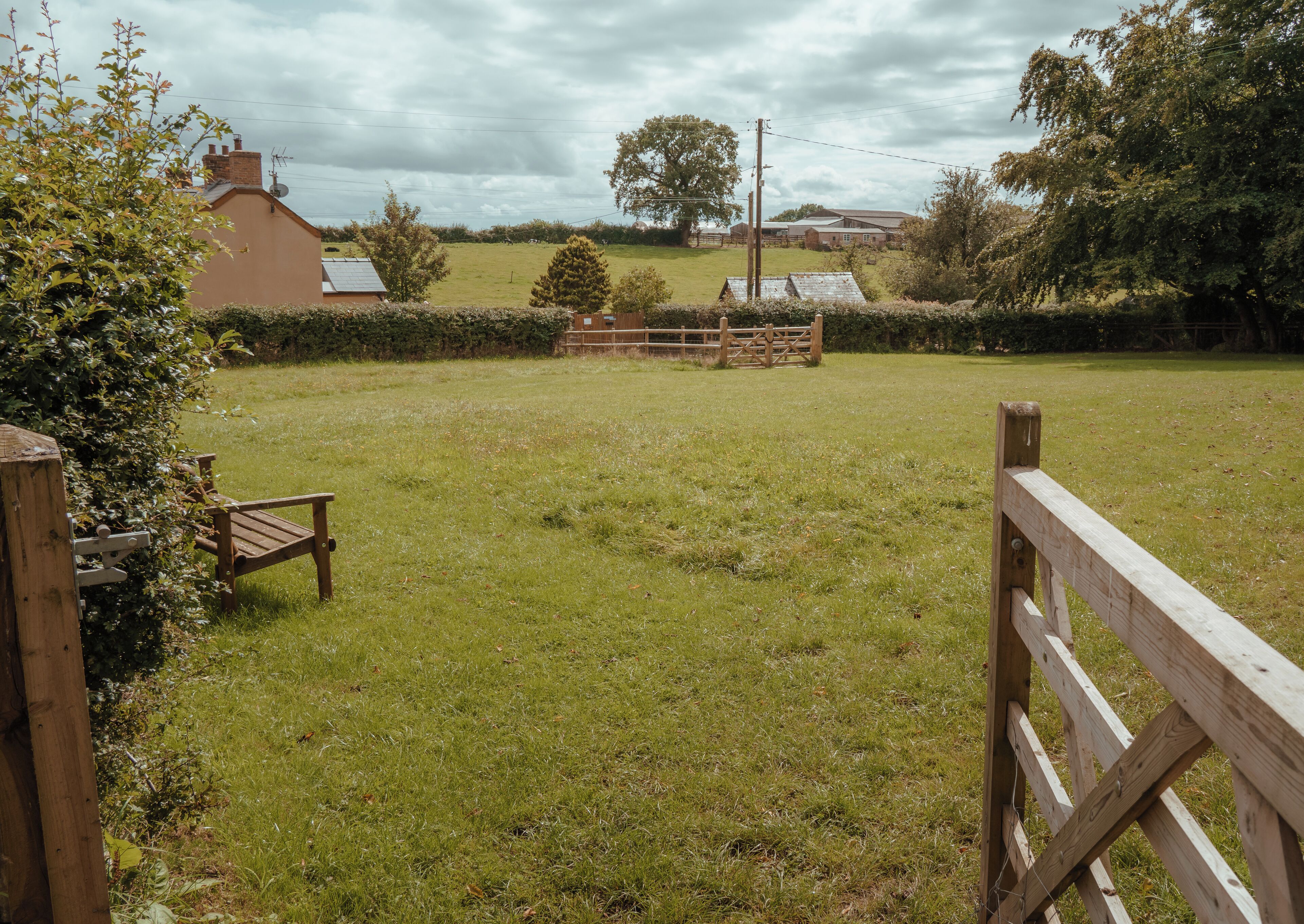 A grassy field with a wooden fence, a bench, and a building in the background.