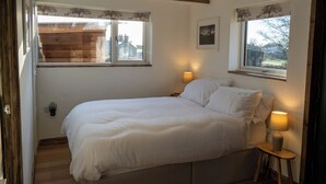 A bedroom with a bed, two bedside lamps, a window with a curtain, and a small table with a lamp.