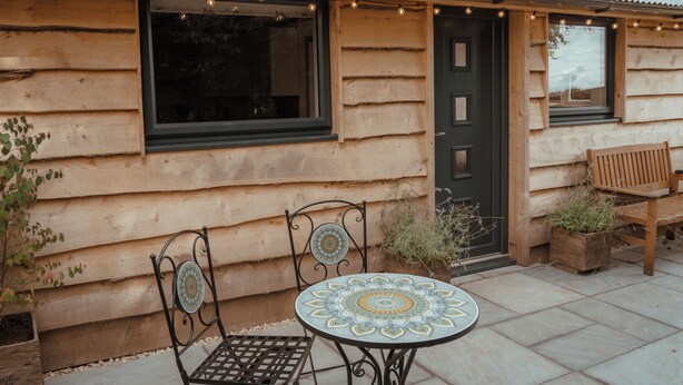 A rustic log cabin with a wooden door, a window, and a small patio area with a table and chairs.