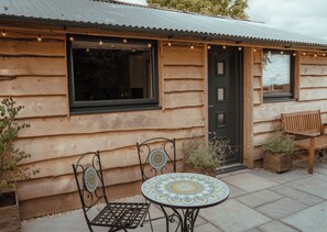 A rustic log cabin with a wooden door, a window, and a small patio area with a table and chairs.