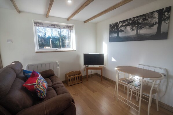 A living room with a brown sofa, a small wooden table, a TV on a stand, and a painting of trees on the wall.
