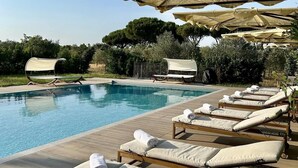 A poolside area with lounge chairs and umbrellas. - Tenuta Fiumara (Grosseto)