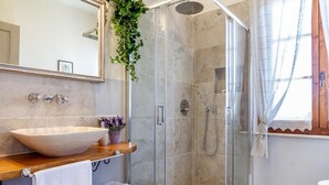 A modern bathroom with a large mirror, a vessel sink, a glass-enclosed shower, and a window with curtains. - Tenuta Fiumara (Grosseto)
