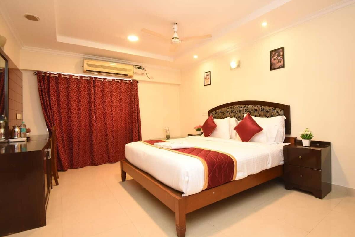 A hotel room with a wooden bed, red curtains, a desk with a chair, an air conditioning unit, and a small bedside table with a plant.