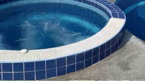 A large, circular swimming pool with a tiled edge, surrounded by a low wall and palm trees. - Surin Dreambeach View 4 (Thap Sakae)