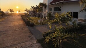A house with a red-tiled roof, a white exterior, and a paved driveway leading to a grassy area with palm trees. - Surin Dreambeach View 4 (Thap Sakae)