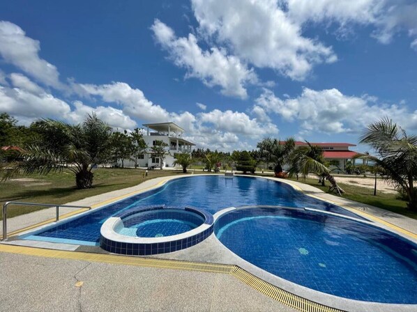 A large outdoor swimming pool with a circular hot tub, surrounded by palm trees and a clear blue sky. - Surin Dreambeach View 4 (Thap Sakae)