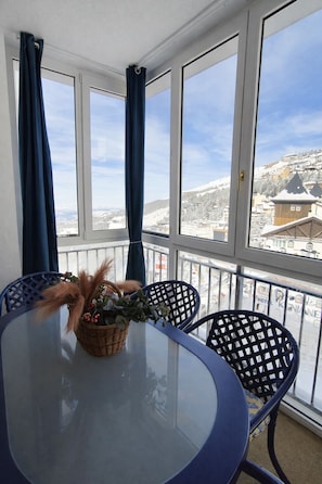 A room with a round glass table, two blue chairs, and a view of a snowy landscape through large windows.