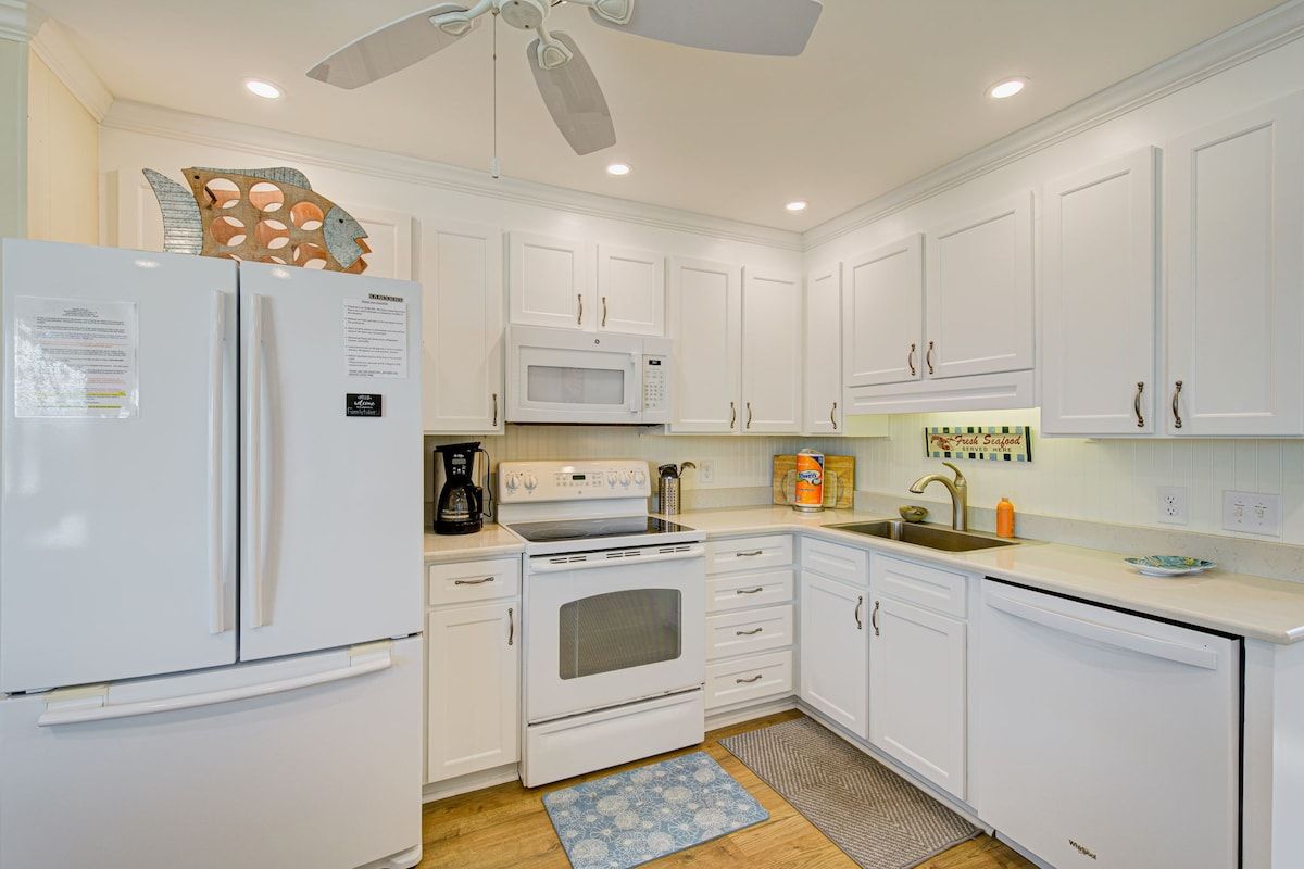 A kitchen with white cabinets, a refrigerator, a microwave, an oven, and a sink.