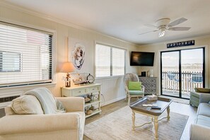 A living room with a sofa, armchair, coffee table, and a television. There is a balcony with a view. - 2BR/2B Oceanfront & Inlet View Gated w/pool (North Myrtle Beach)