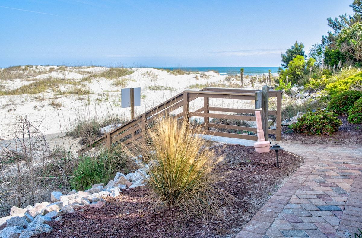 A wooden deck with a metal railing overlooking a beach.