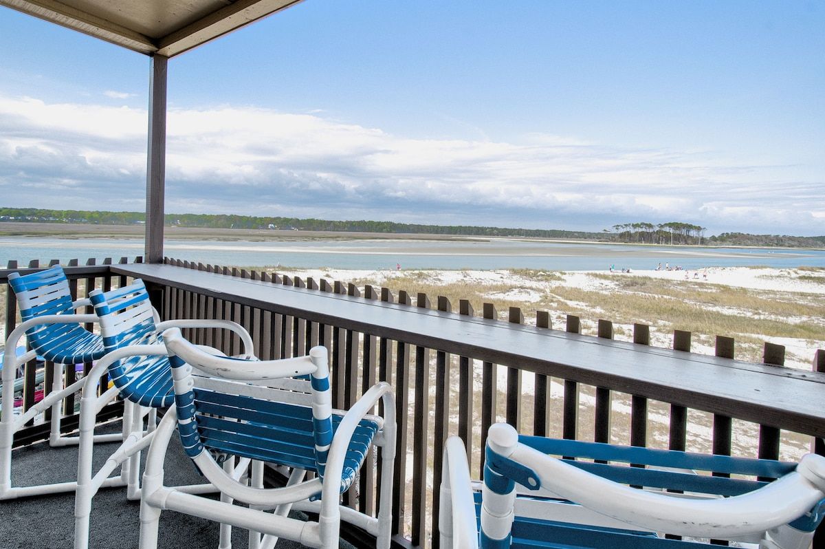 A covered outdoor seating area with chairs and a view of a beach and water.