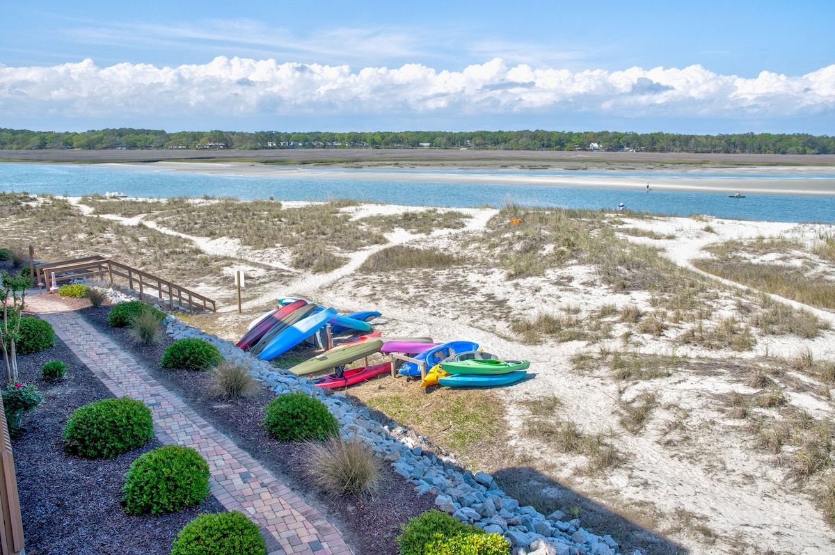 A beach with kayaks and a wooden walkway leading to a building.
