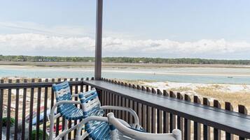 A covered outdoor area with a view of a beach and ocean. There are two chairs and a table.