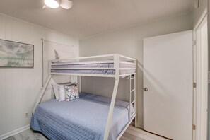 Ein Schlafraum mit Etagenbetten, einer weißen Tür, einem gerahmten Bild an der Wand und einem Lichtschalter.