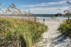Ein Sandweg am Strand führt zum Meer, ein Wegweiser ist sichtbar.