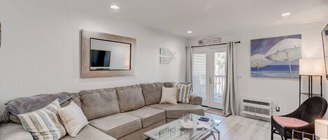 A living room with a sectional sofa, a glass coffee table, and a wicker chair.