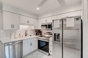 A modern kitchen with white cabinetry, stainless steel appliances, and a patterned floor. - Inlet Facing 1st Floor 2B/2B Condo w/pool (North Myrtle Beach)