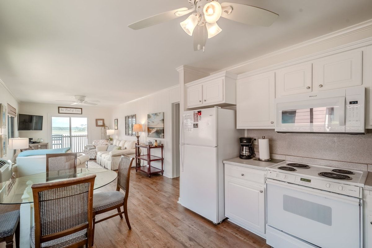 A modern kitchen with white cabinets, a microwave, a stove, and a refrigerator. There is a dining area with a glass table and chairs.