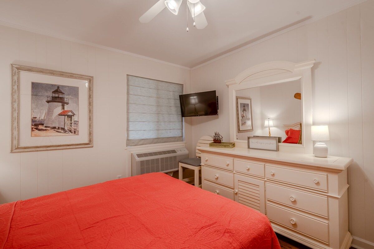 Une chambre à coucher avec un lit, une commode, un téléviseur et des œuvres d’art accrochées au mur.