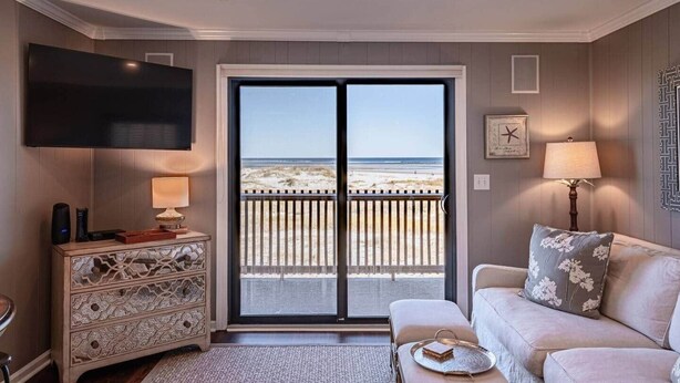 Ein Wohnzimmer mit Fernseher, einer Couch, einem Couchtisch und Blick auf den Strand durch eine Schiebetür.