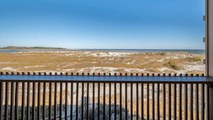Blick vom Balkon auf einen Strand mit Dünen und einem wolkenlosen Himmel.